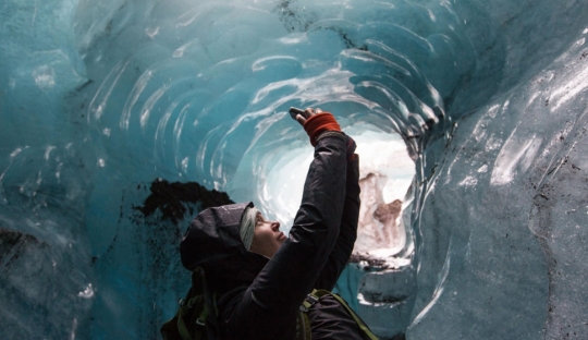 Young female adult standing in an ice cave looking upwards