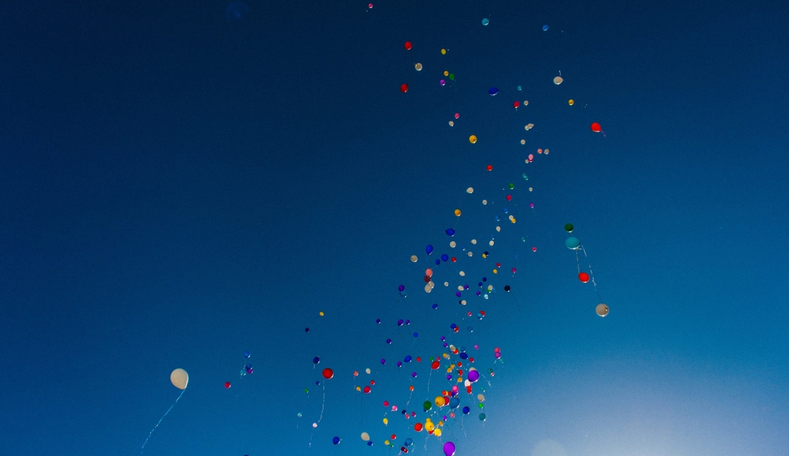 multi coloured balloons floating across a bright blue sky