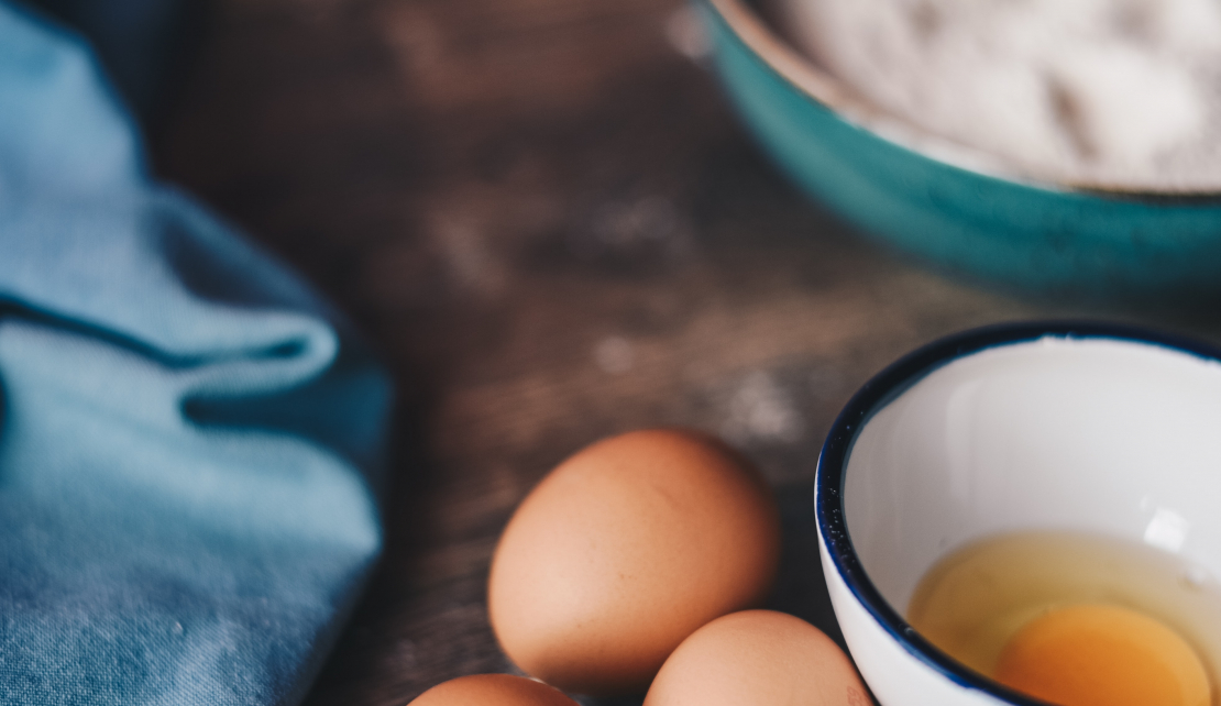 eggs cracked into a mixing bowl and a tea towel on a wooden kitchen bench